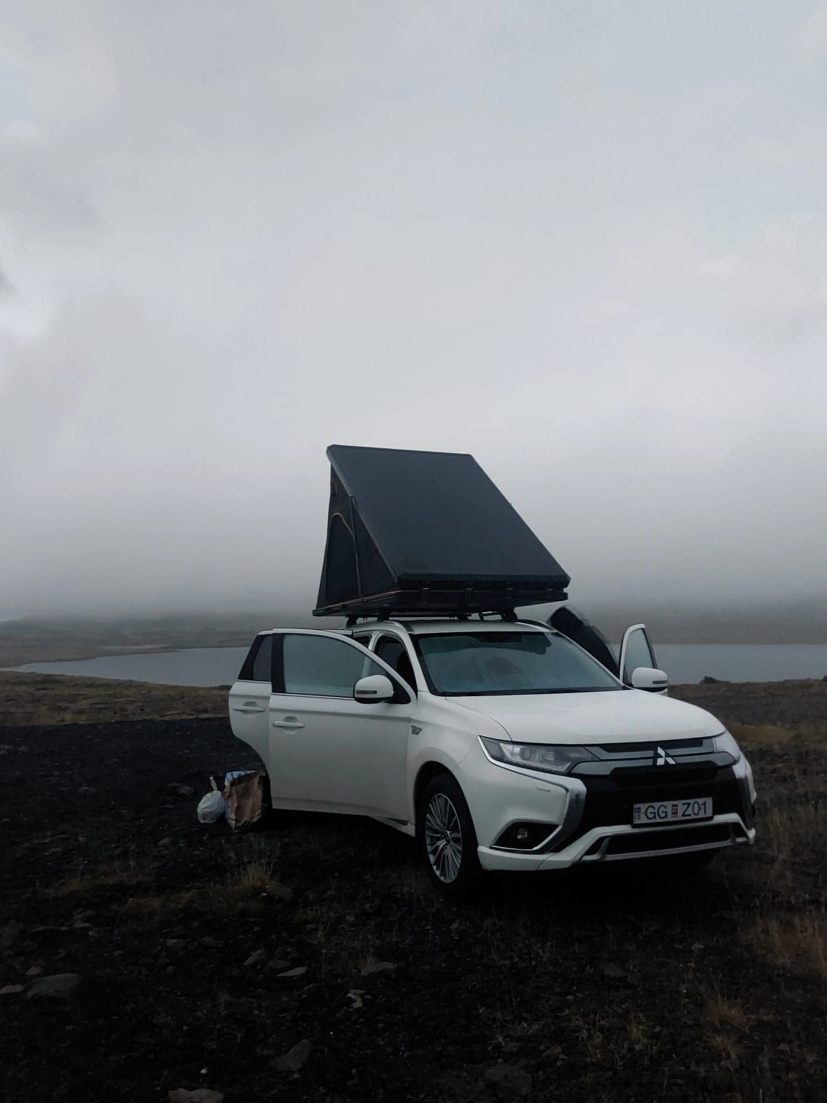 A car with a rooftop tent by a lake under a grey Icelandic sky