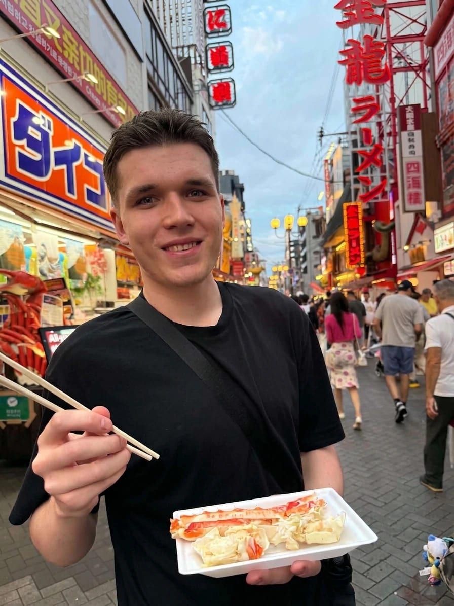 Jakub holding a tray of street food on a busy, neon-lit street in Japan